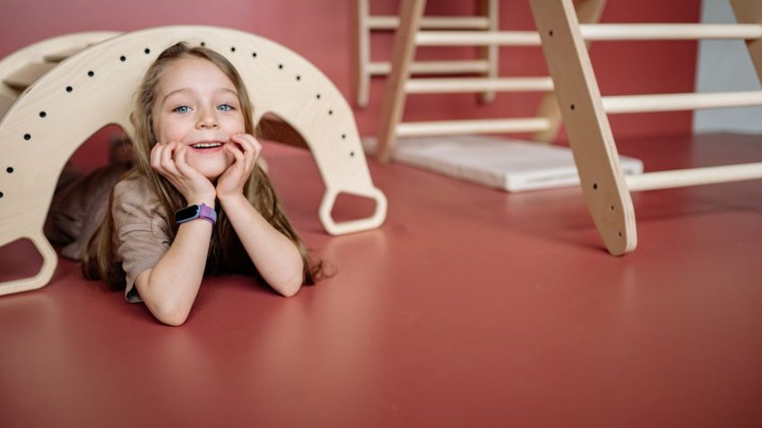 A joyful child playing with a wooden toy bridge indoors, smiling and having fun.